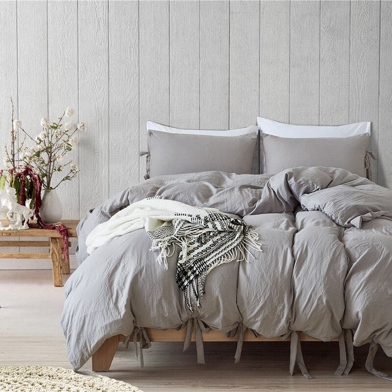 Bowtie Lace up Duvet Cover set in light gray.  The bed is layered with matching pillow shams that are included in this set and a small throw blanket in black and white with a coastal setting background.