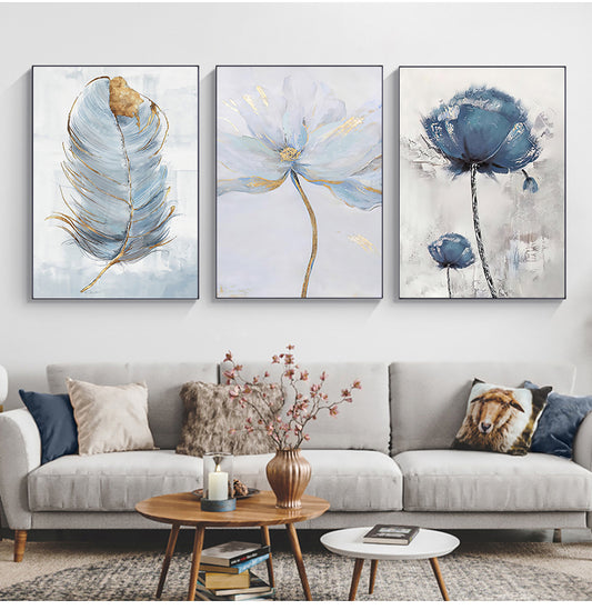 Gallery wall showing 3 designs of the blue gray flower and feather collection canvas wall art centered on a living room wall over a sofa.