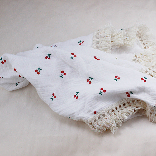 Bamboo and Cotton Muslin Baby Swaddle Blanket.  White background with small red cherry bunches scattered throughout the design.  This swaddle blanket is completed with creamy beige fringed edging.  Available in 2 sizes 47"X40" or 31"X25".