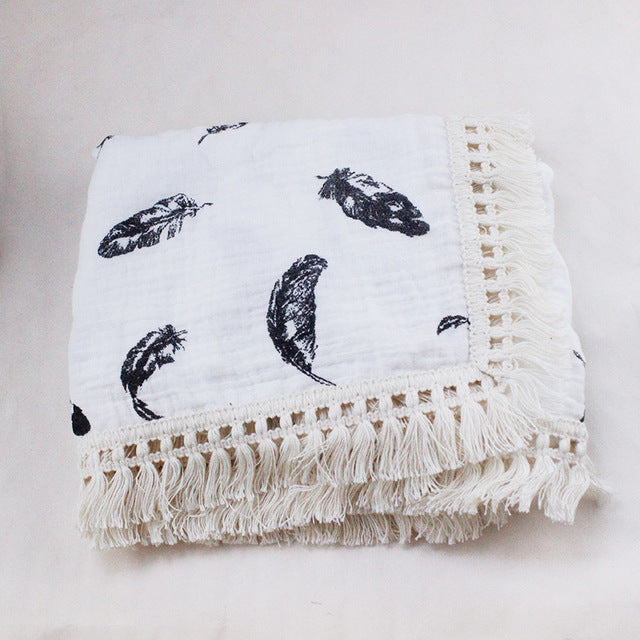 Bamboo and Cotton Muslin Baby Swaddle Blanket.  White background with large bluish-black feathers randomly scattered throughout the blanket.  This swaddle blanket is completed with a creamy white fringed edging.  Available in 2 sizes  47"X40" or 31"X25".