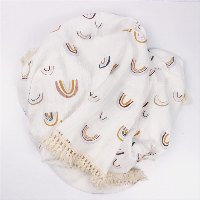 Bamboo and Cotton Muslin Baby Swaddle Blanket.  White background with randomly scattered woodland look rainbows in taupe, golds, and pale blue.  This blanket comes complete with a creamy beige fringed edging.  Available in 2 sizes  47"X40" and 31"X25".